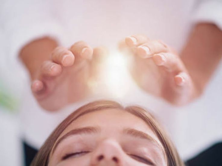 Hands hovering above the recipient&rsquo;s forehead during a Reiki session, with a soft glow of light between them.